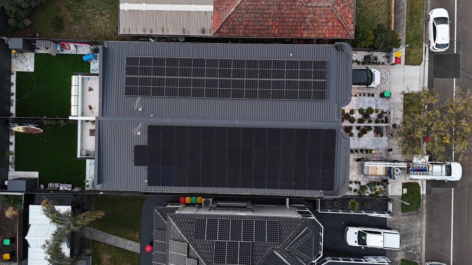 Aerial view of a large solar array across two roof sections, with the Infinite van and gear set up on site