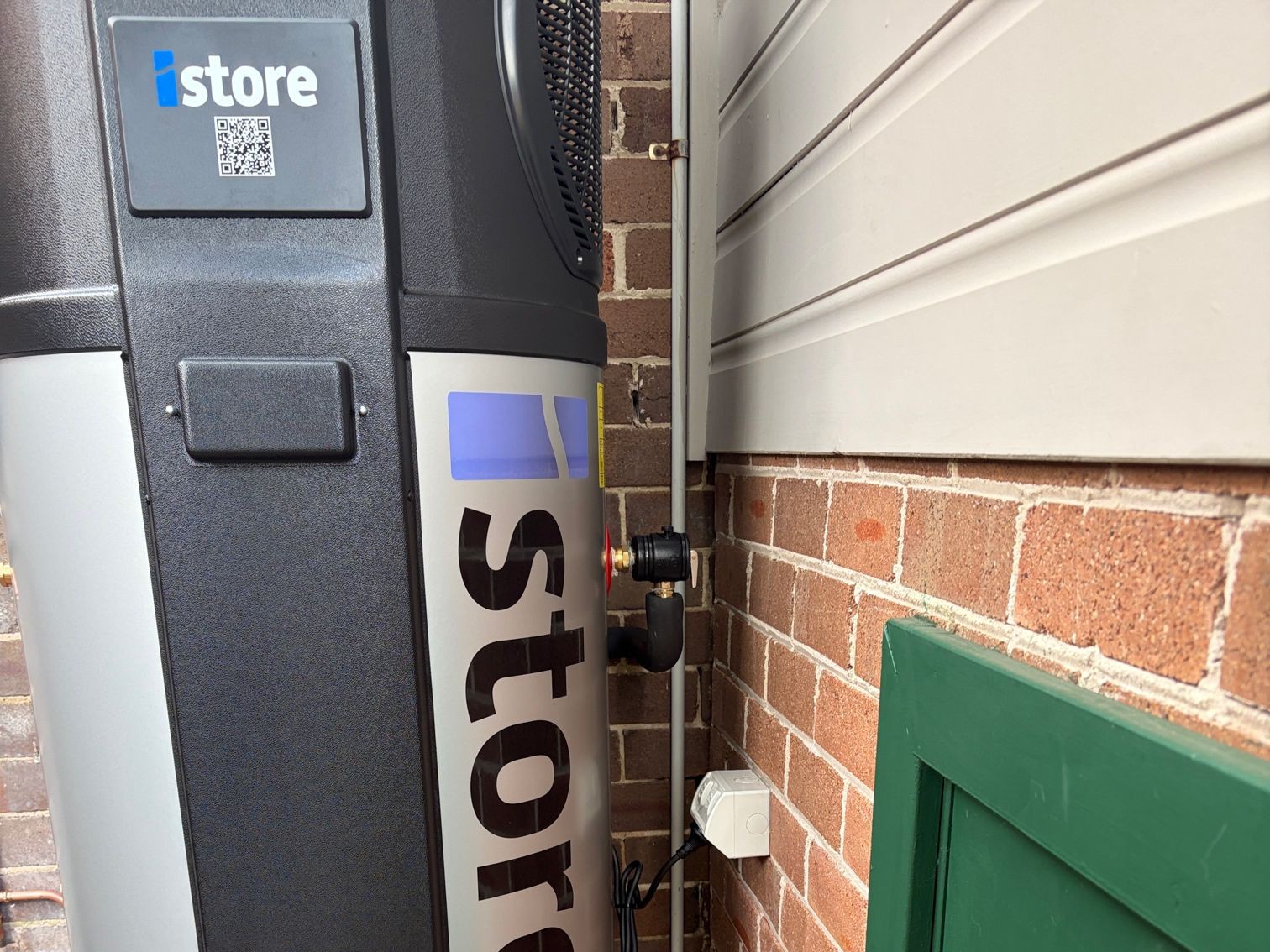 Freshly installed iStore heat pump hot water unit against a brick wall, showing the iStore logo and QR code