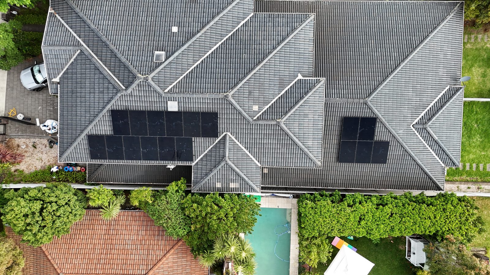 Aerial view of a diamond-shaped tiled roof with solar panels next to a pool