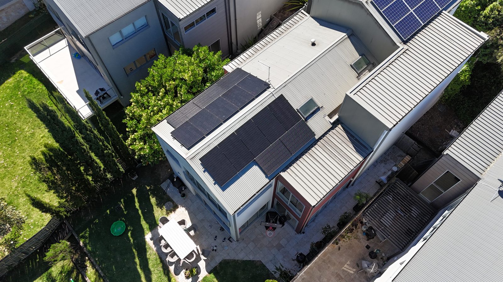 Aerial view of a multi-level home with solar panels on a sunlit flat roof