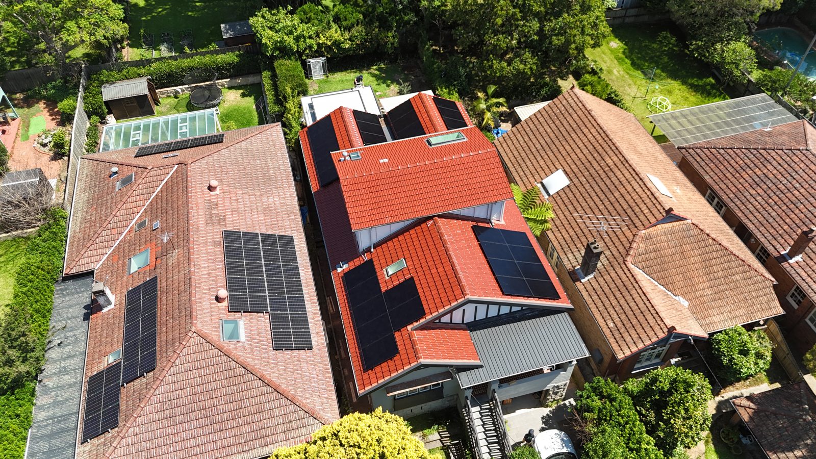 Aerial view of a red-roofed home with solar panels and a palm tree in the yard