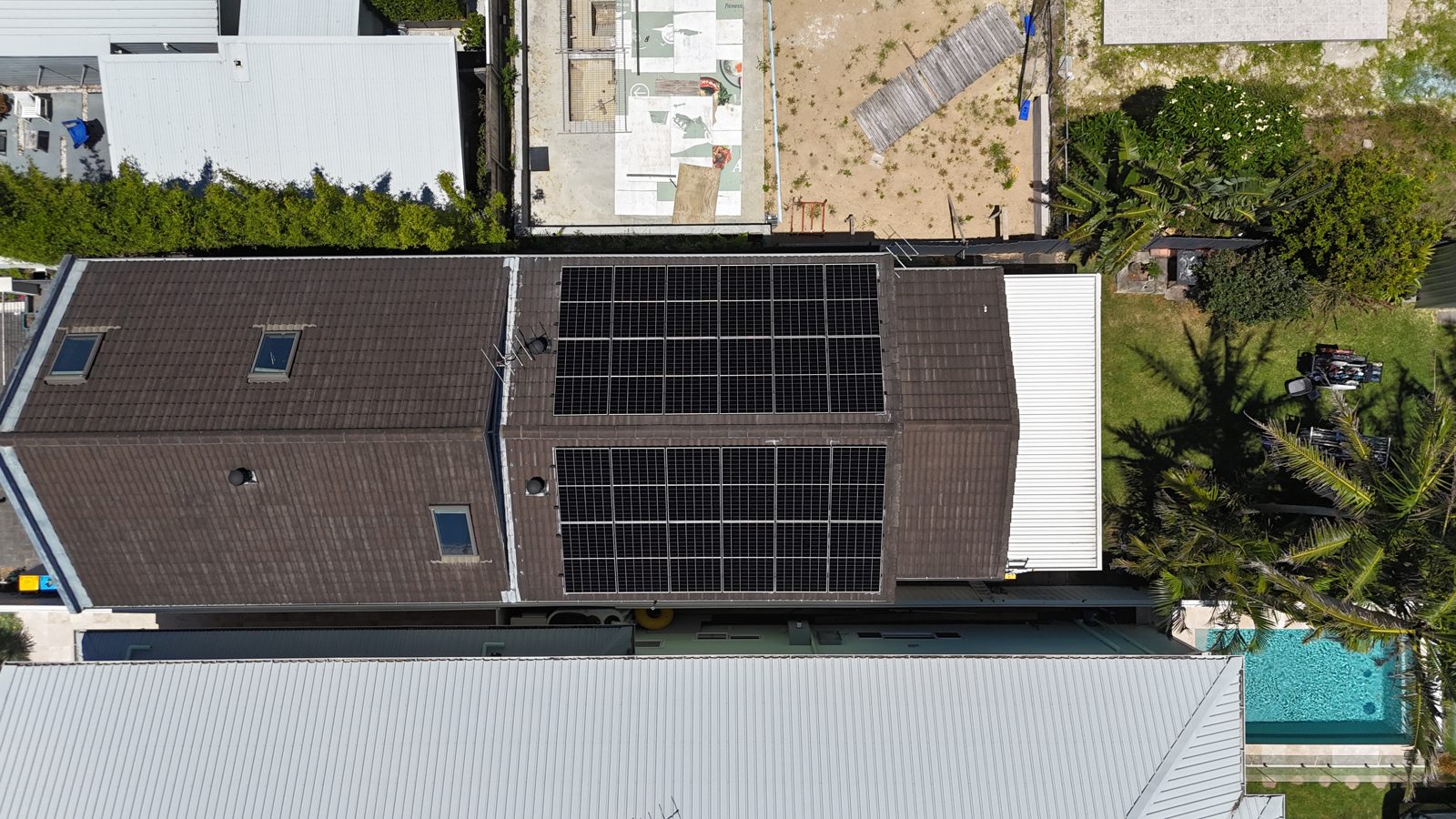 Aerial view of a flat skillion roof covered in solar panels next to a pool