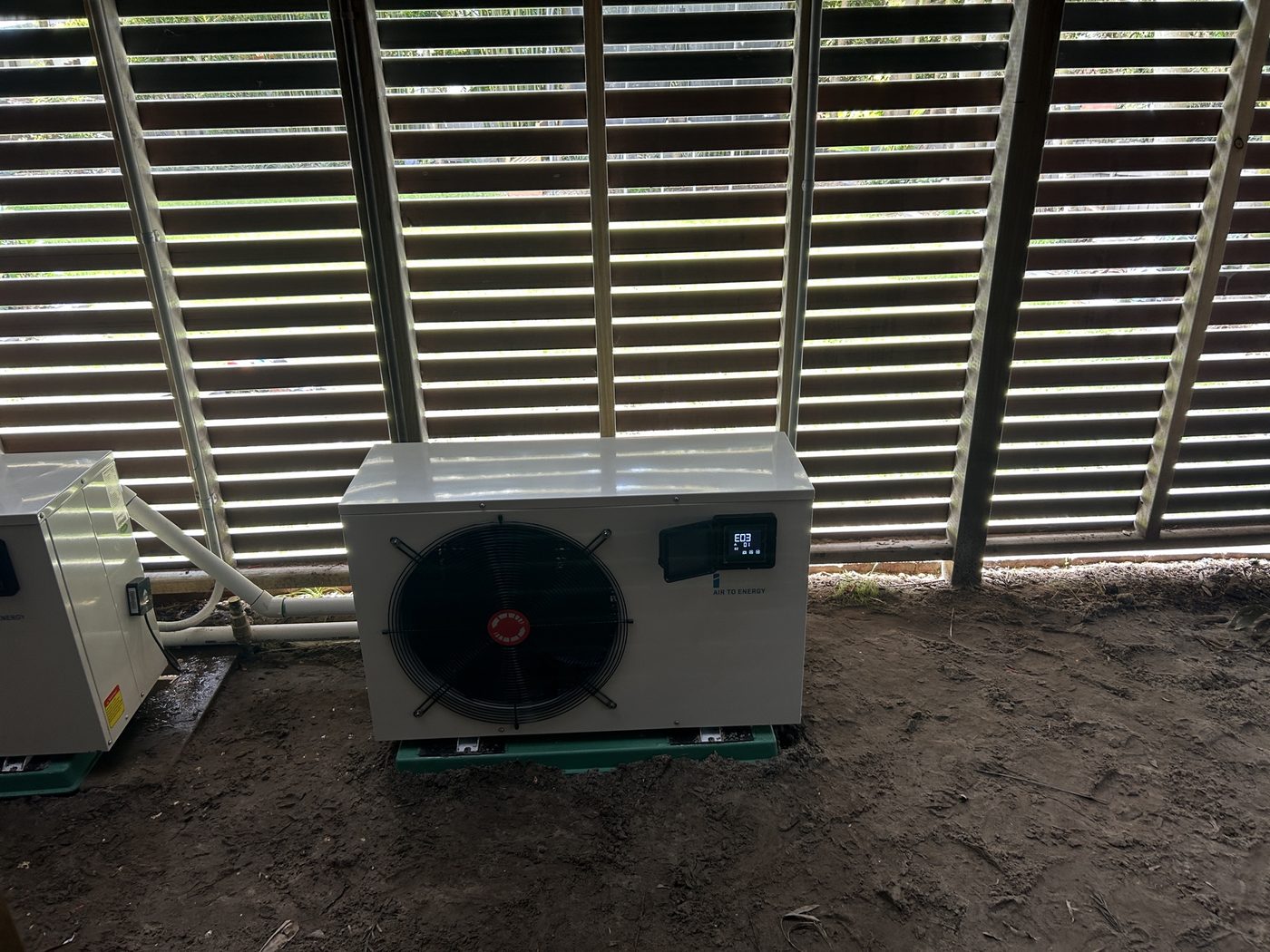 iStore pool heat pump unit installed against a slatted fence