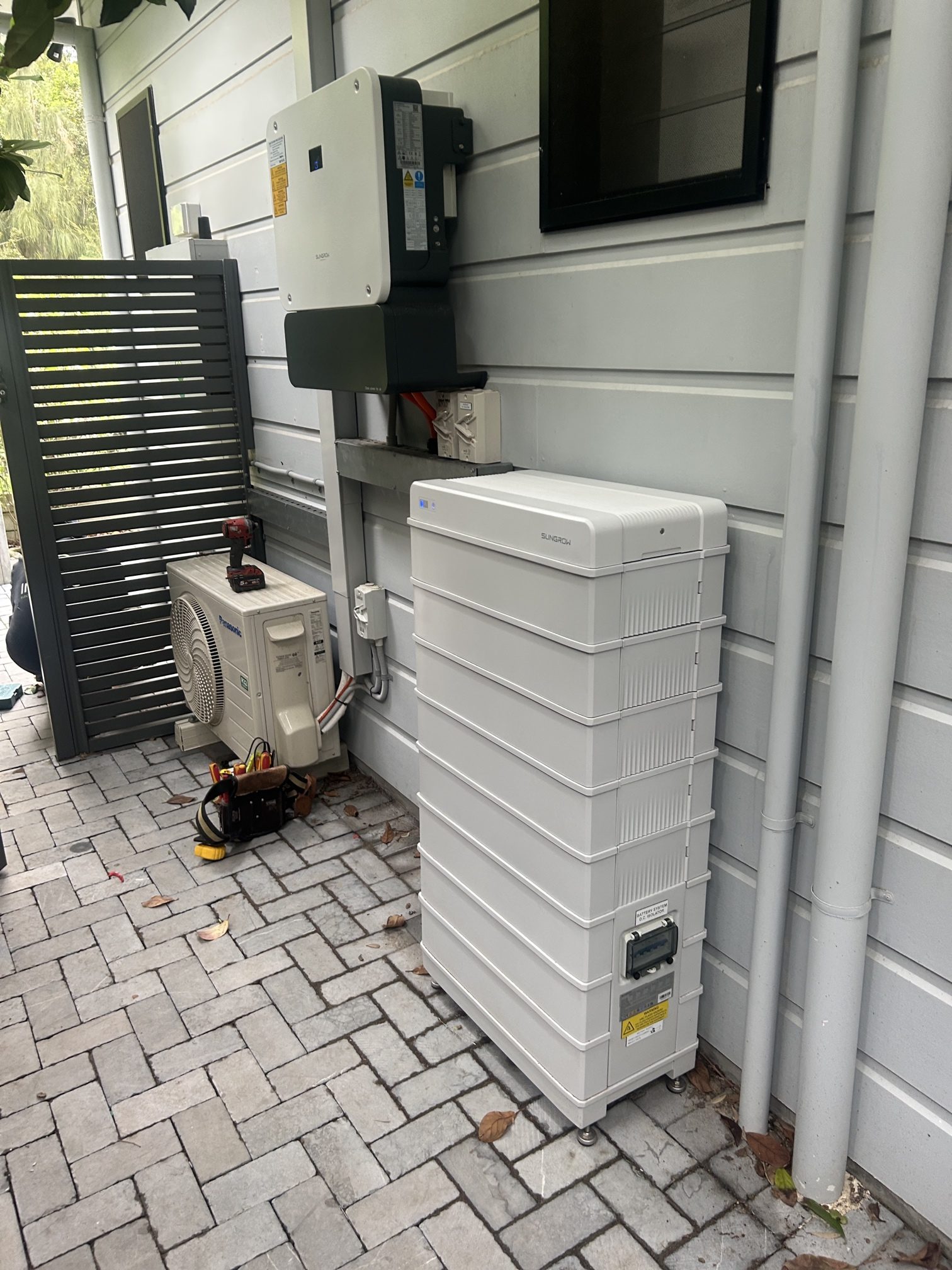 Sungrow inverter and battery stack installed outside a home, alongside an outdoor air conditioning unit