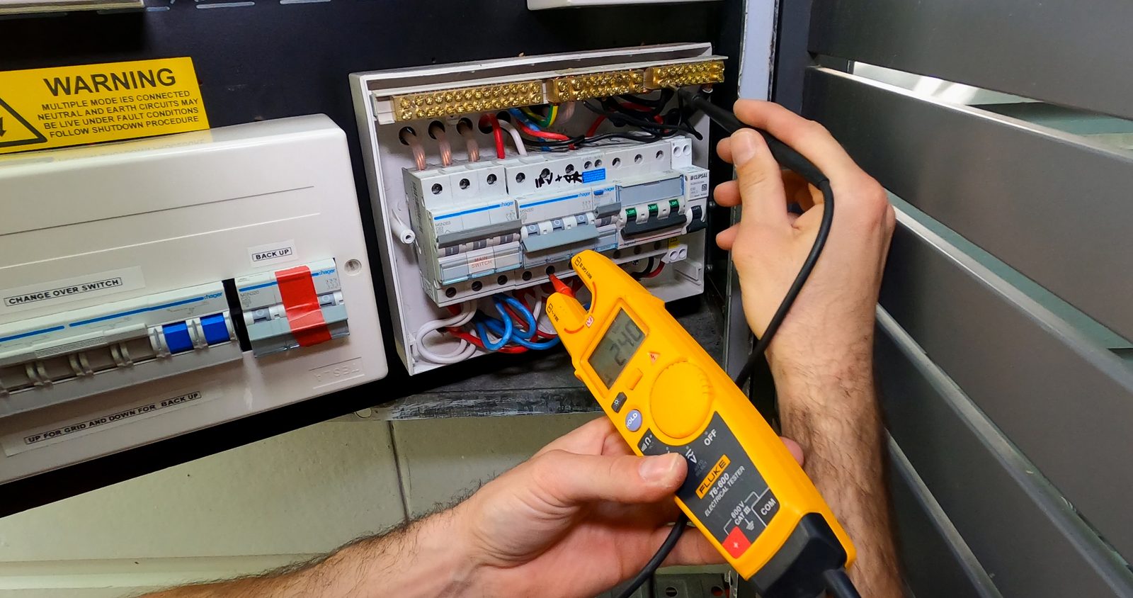 Electrician testing an open switchboard with a Fluke multimeter